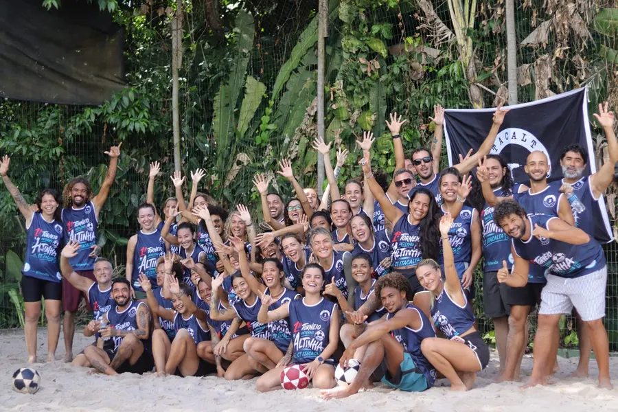Grupo de atletas da 1ª edição reunido na areia com a bandeira do Itacalta